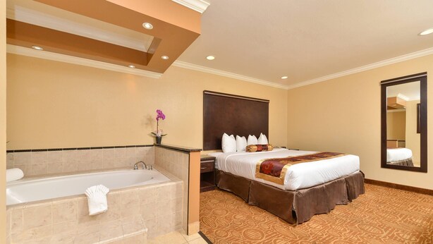 A hotel room with a large bed, a separate bathroom with a bathtub, and a mirror on the wall.