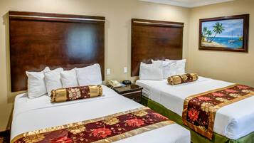 A hotel room with two beds, each with a wooden headboard, white bedding, and a floral bedspread. There is a painting of a beach scene on the wall.