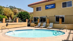 A pool area with lounge chairs, a sign for Rodeway Inn, and a building with a tiled roof.