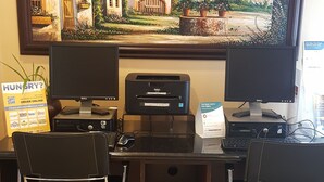 A home office setup with a desktop computer, two office chairs, a printer, and a desk with a tray of books.