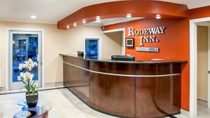 A reception desk with a glass top, a potted plant, and a sign for Rodeway Inn.