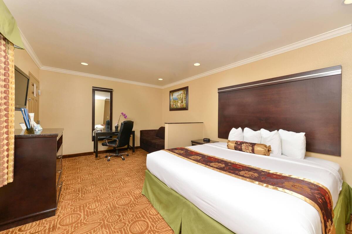 A hotel room with a large bed, a desk, a chair, a mirror, and a picture on the wall.