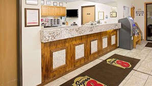 A hotel reception area with a marble counter, wooden paneling, a television, and a vending machine.