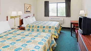A hotel room with two beds, a desk with a television, a window with curtains, and a wall-mounted air conditioner.