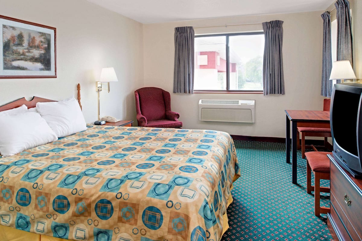 Ein Hotelzimmer mit einem großen Bett, einem Schreibtisch, einem Stuhl, einem Fernseher und einem Fenster mit Vorhängen.