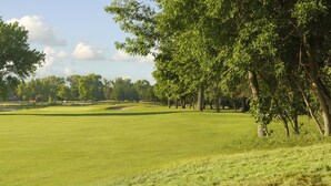 A golf course with a water body, trees, and a clear sky.