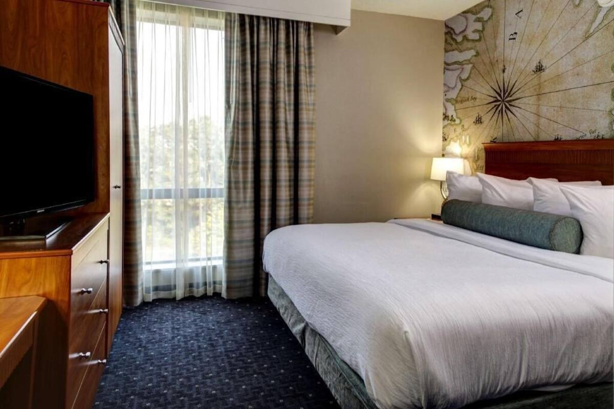 A hotel room with a large bed, a flat-screen TV, a map wall, and a window with curtains.