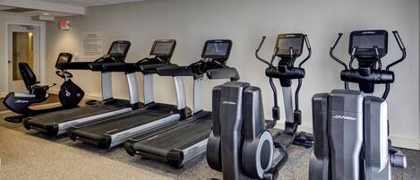 A row of cardio machines including treadmills and elliptical trainers in a gym.