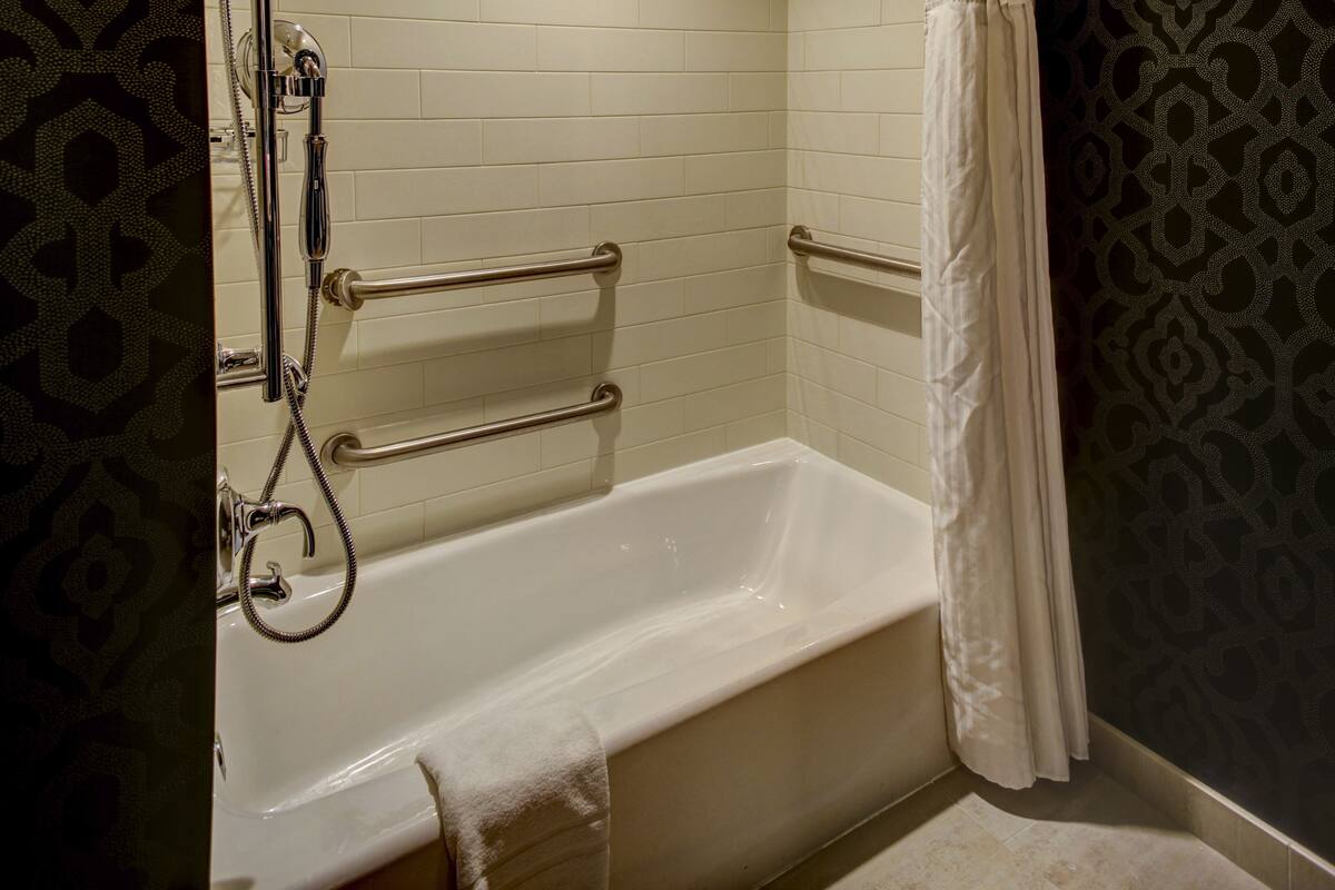 A bathroom with a white bathtub, grab bars, and a showerhead.
