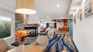 A modern interior with a stone fireplace, a dining area with a vase of flowers, and a blue patterned carpet. - Fairfield Inn & Suites by Marriott San Francisco Pacifica (Pacifica)