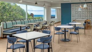 A modern restaurant with a view of the ocean, featuring blue seating, round tables, and a patterned wall. - Fairfield Inn & Suites by Marriott San Francisco Pacifica (Pacifica)