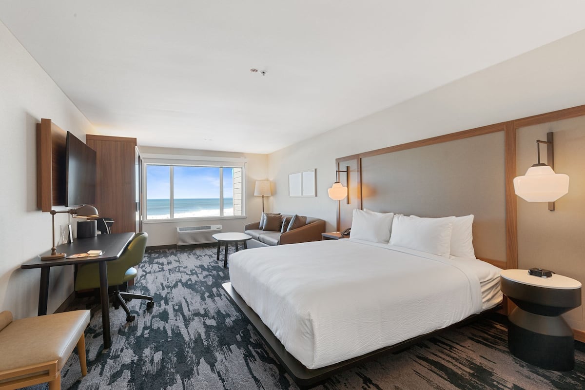 A hotel room with a large bed, a desk, a chair, a sofa, and a TV.