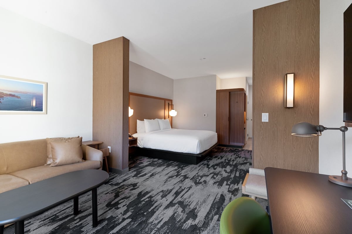 A hotel room with a bed, a sofa, a desk, and a lamp.