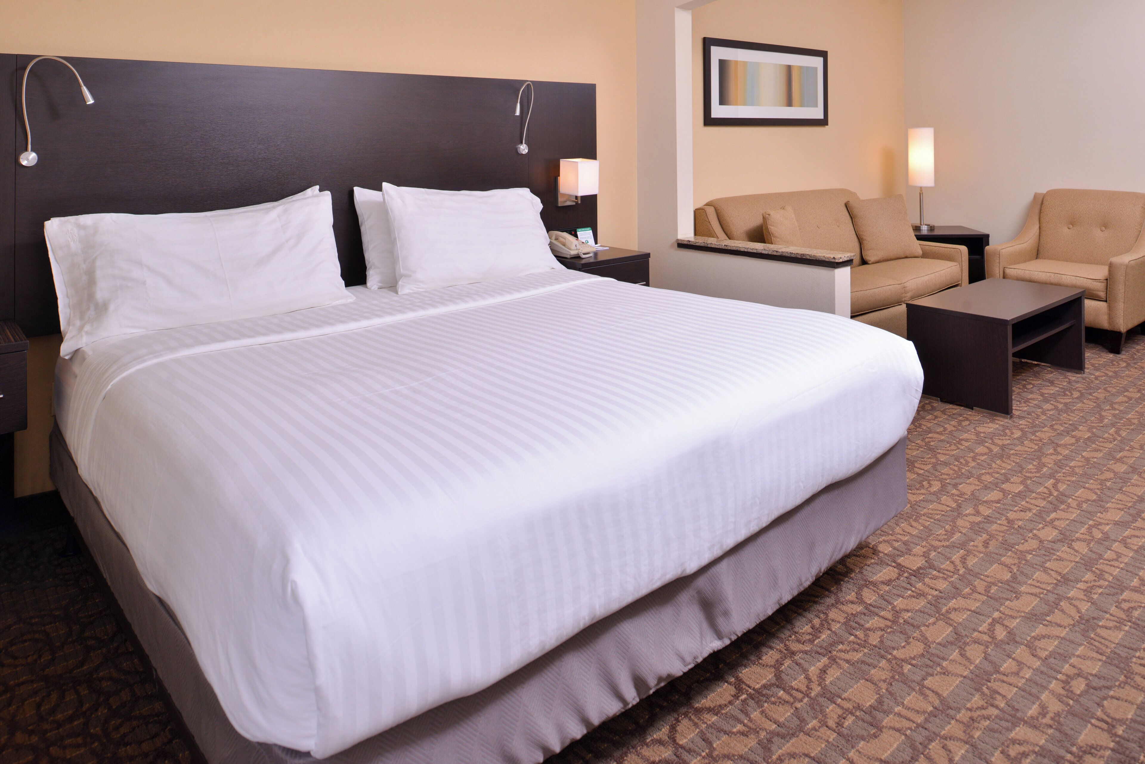 A hotel room with a large bed, a desk, two chairs, and a nightstand.