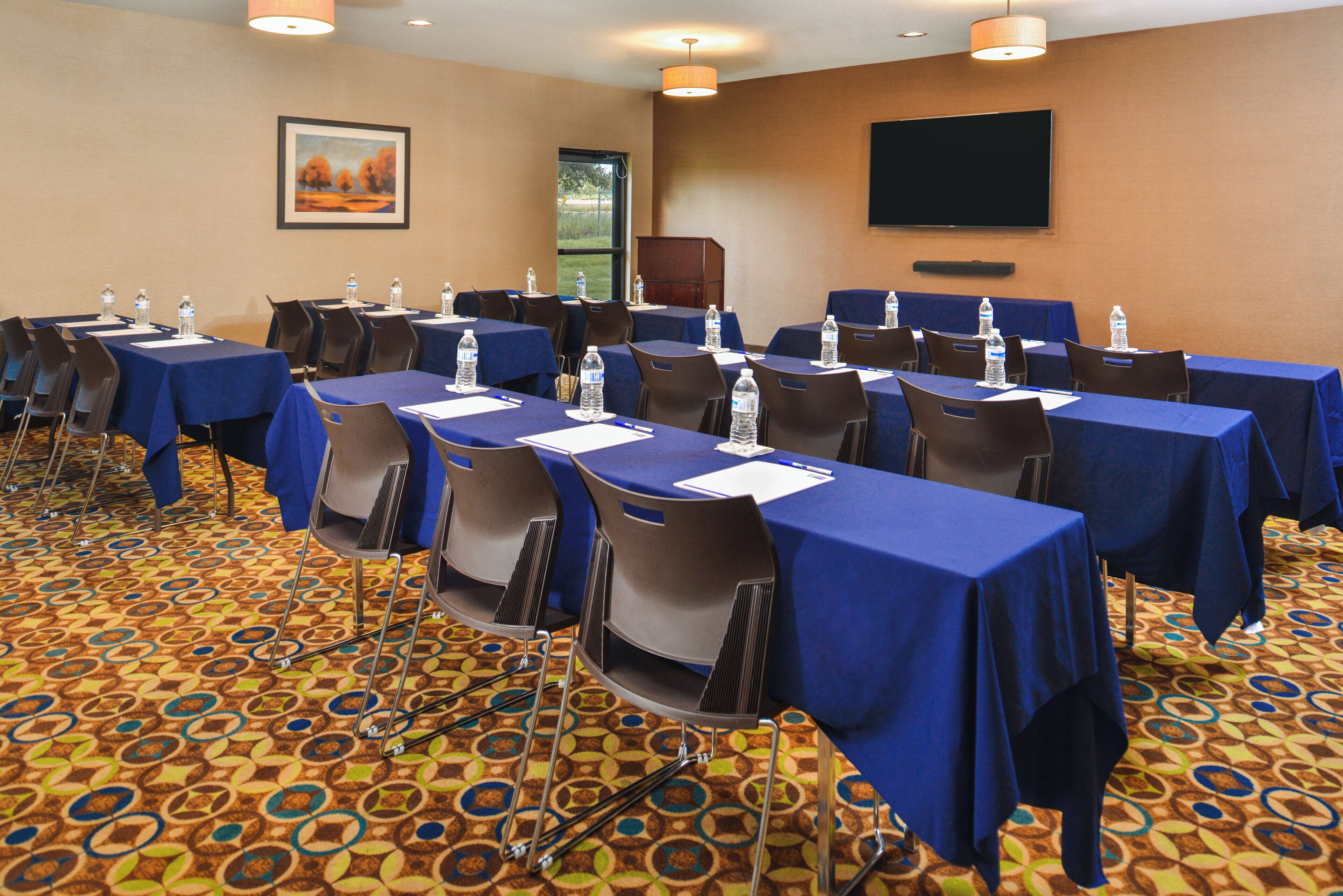 A conference room with tables, chairs, water bottles, and a painting on the wall.