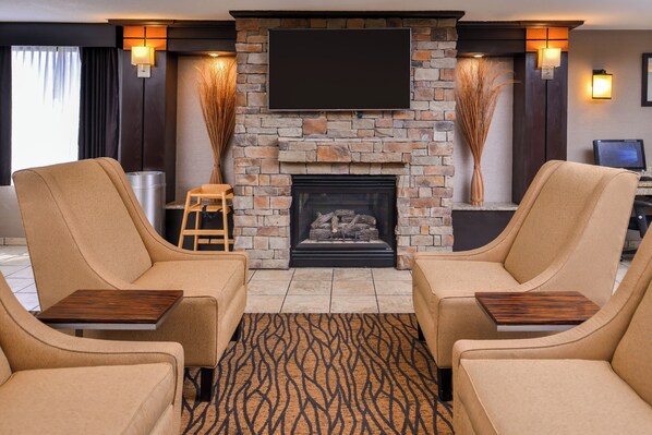 A living room with a stone fireplace, two armchairs, a small wooden ladder, and a flat-screen TV mounted above the fireplace.