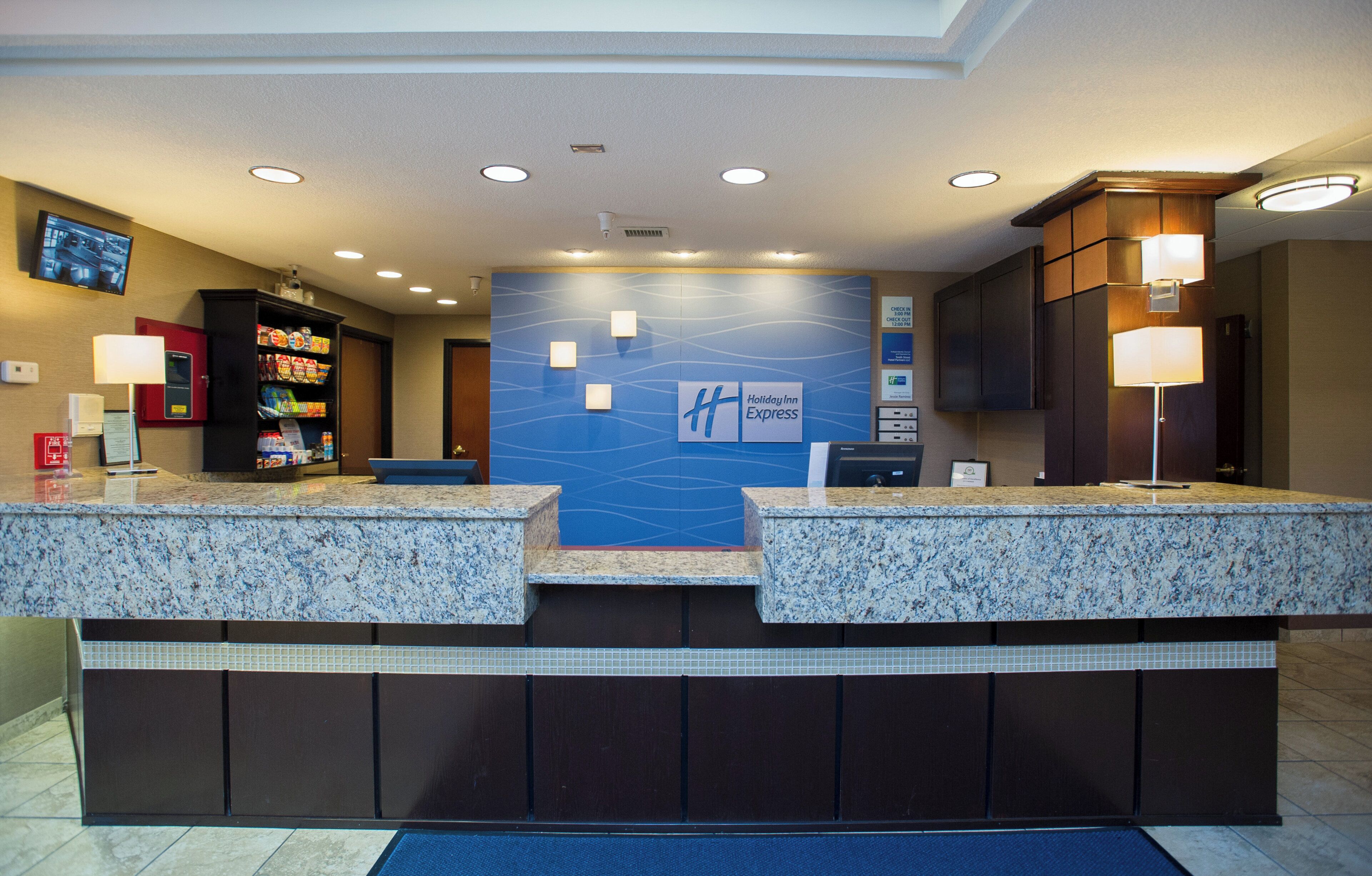 A hotel reception area with granite counters, a blue wall with the Holiday Inn Express logo, and a security camera on the ceiling.