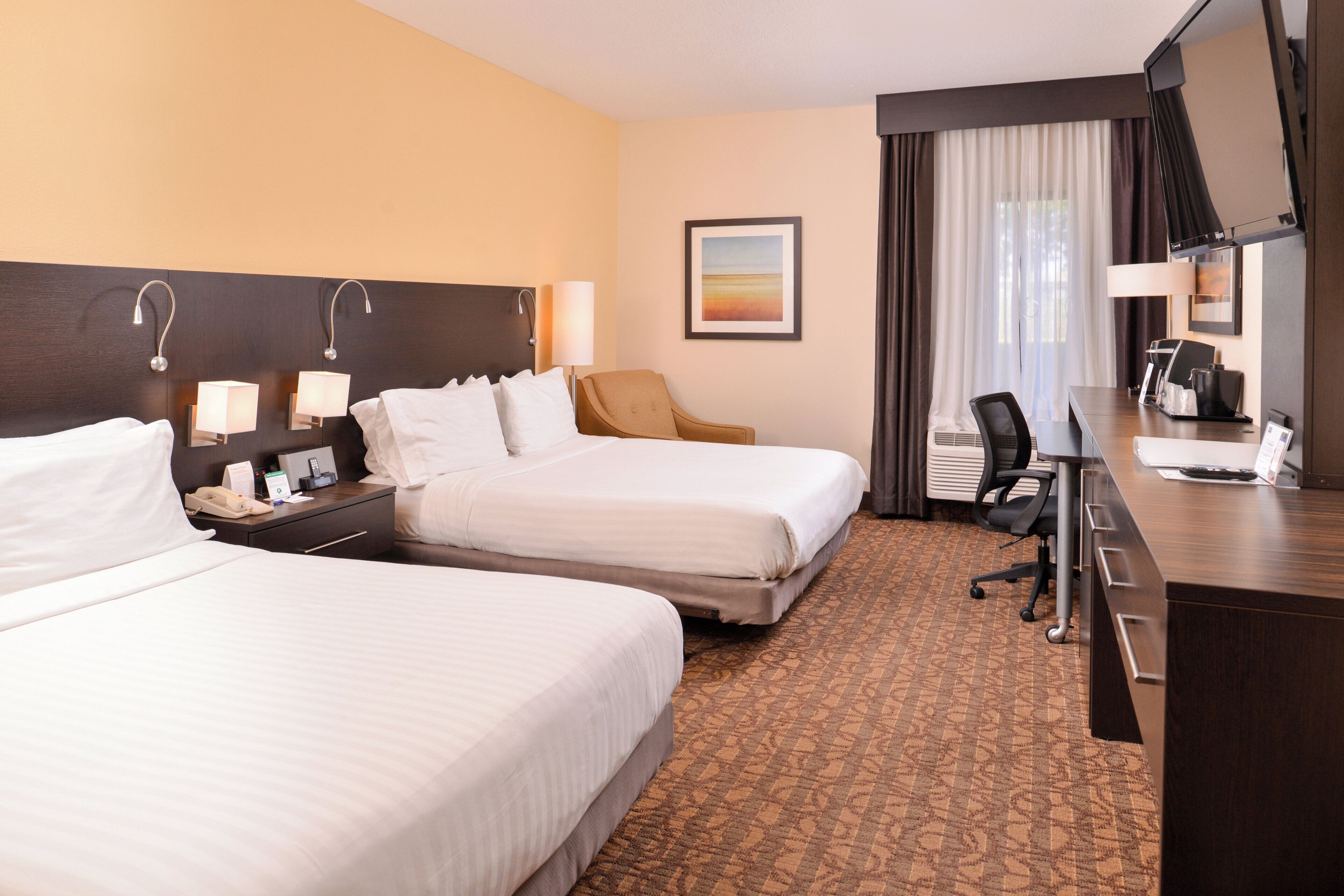 A hotel room with two beds, a desk, a chair, a desk lamp, a telephone, and a painting on the wall.