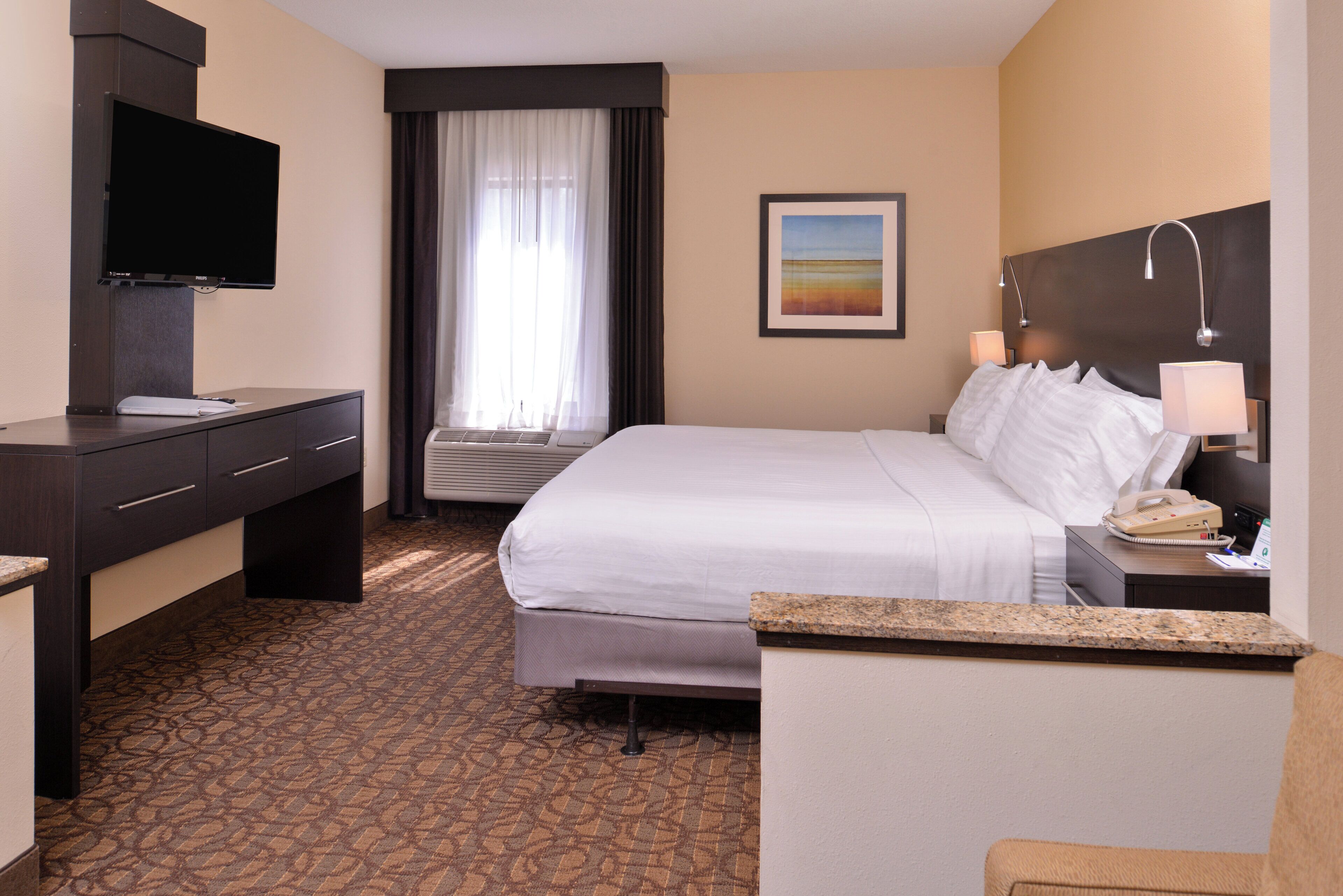 Een hotelkamer met een bed, een bureau, een flatscreen-tv, een raam met gordijnen, een schilderij aan de muur en een telefoon.