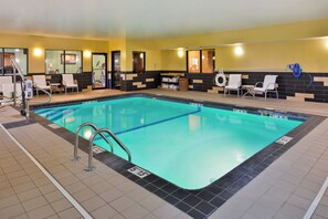 An indoor swimming pool with a tiled floor, a lifeguard stand, and lounge chairs.