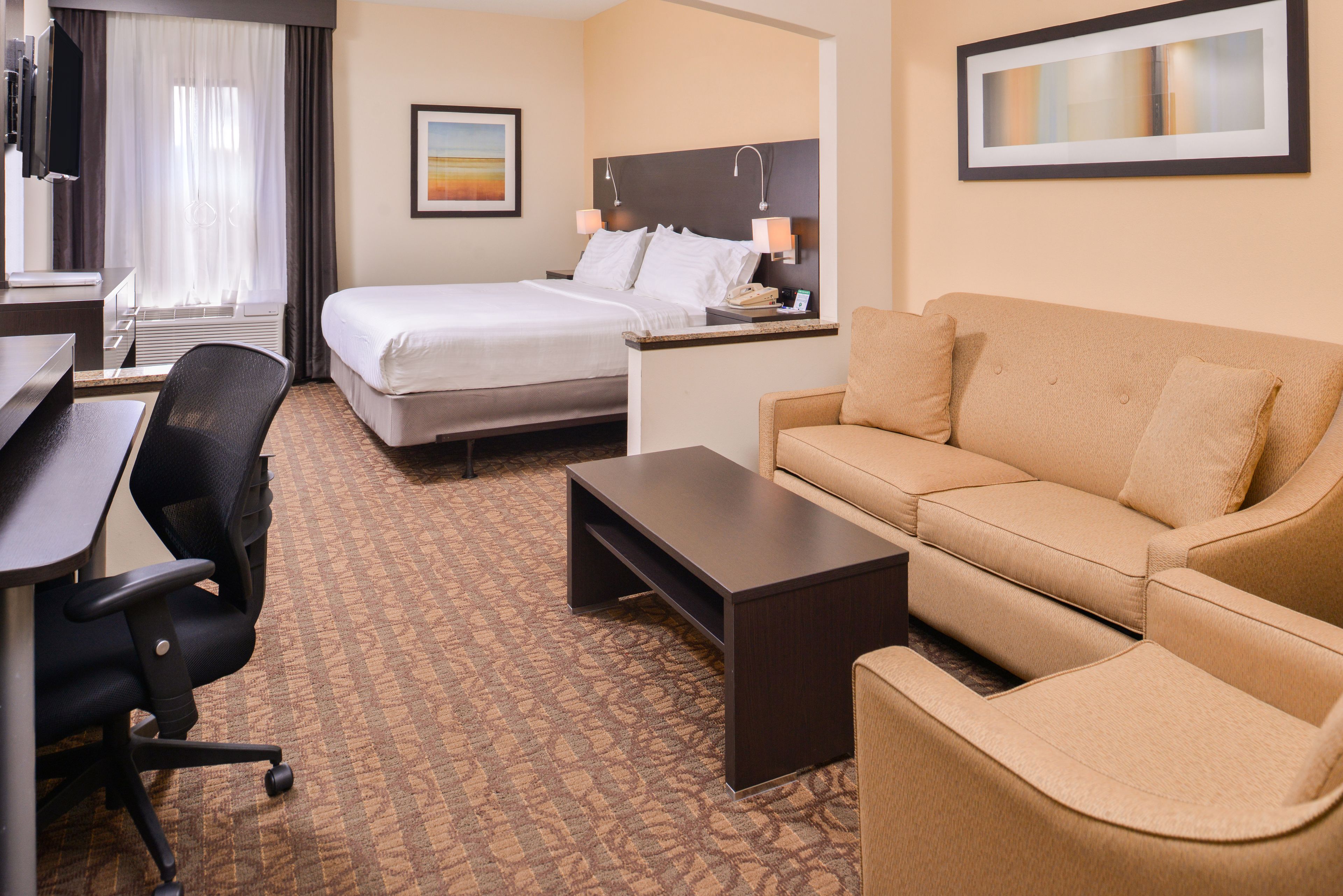 A hotel room with a bed, a desk, a chair, a sofa, and a coffee table.