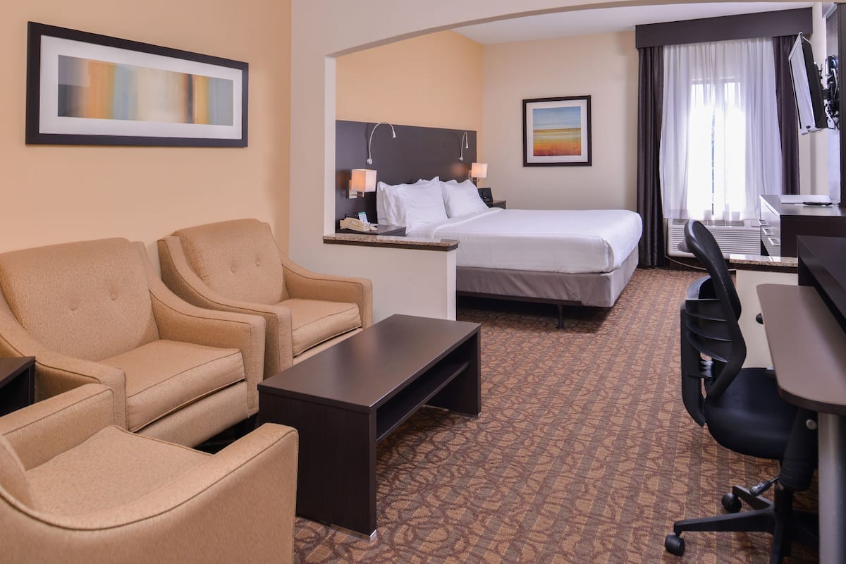 A hotel room with a bed, two armchairs, a desk, and a computer.