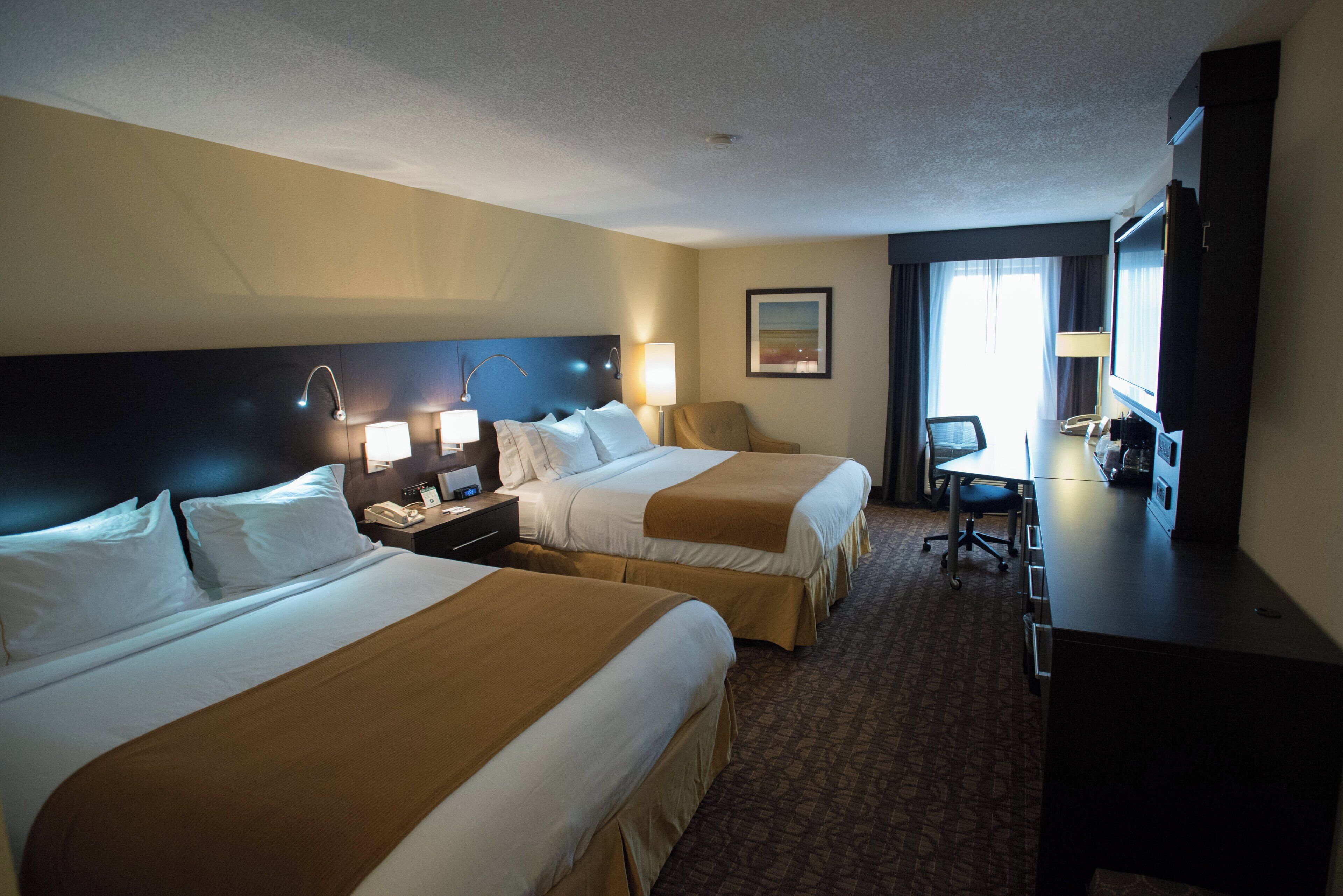 A hotel room with two beds, a desk, a chair, a TV, and a painting on the wall.