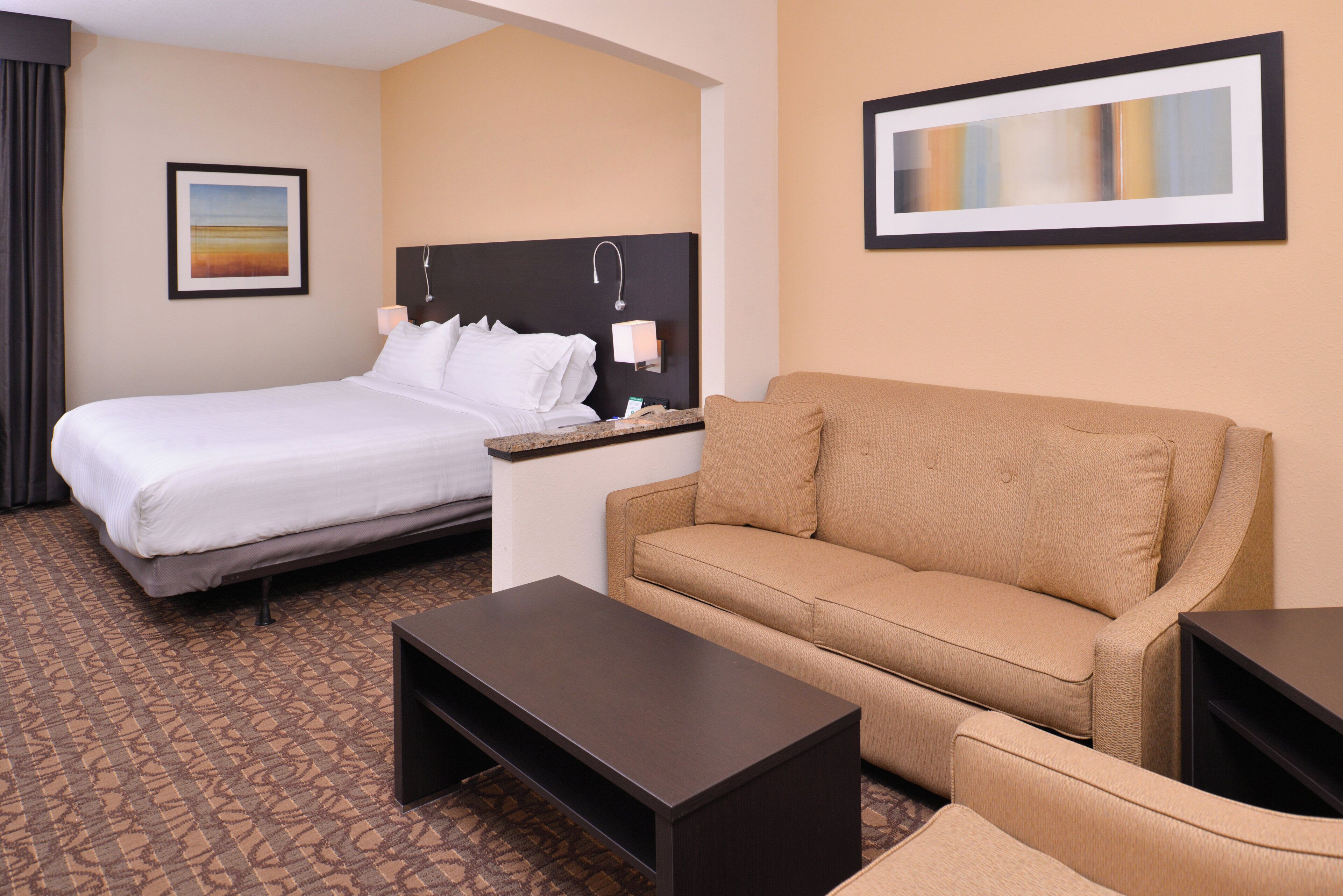 A hotel room with a bed, a sofa, a coffee table, a nightstand, and a painting on the wall.