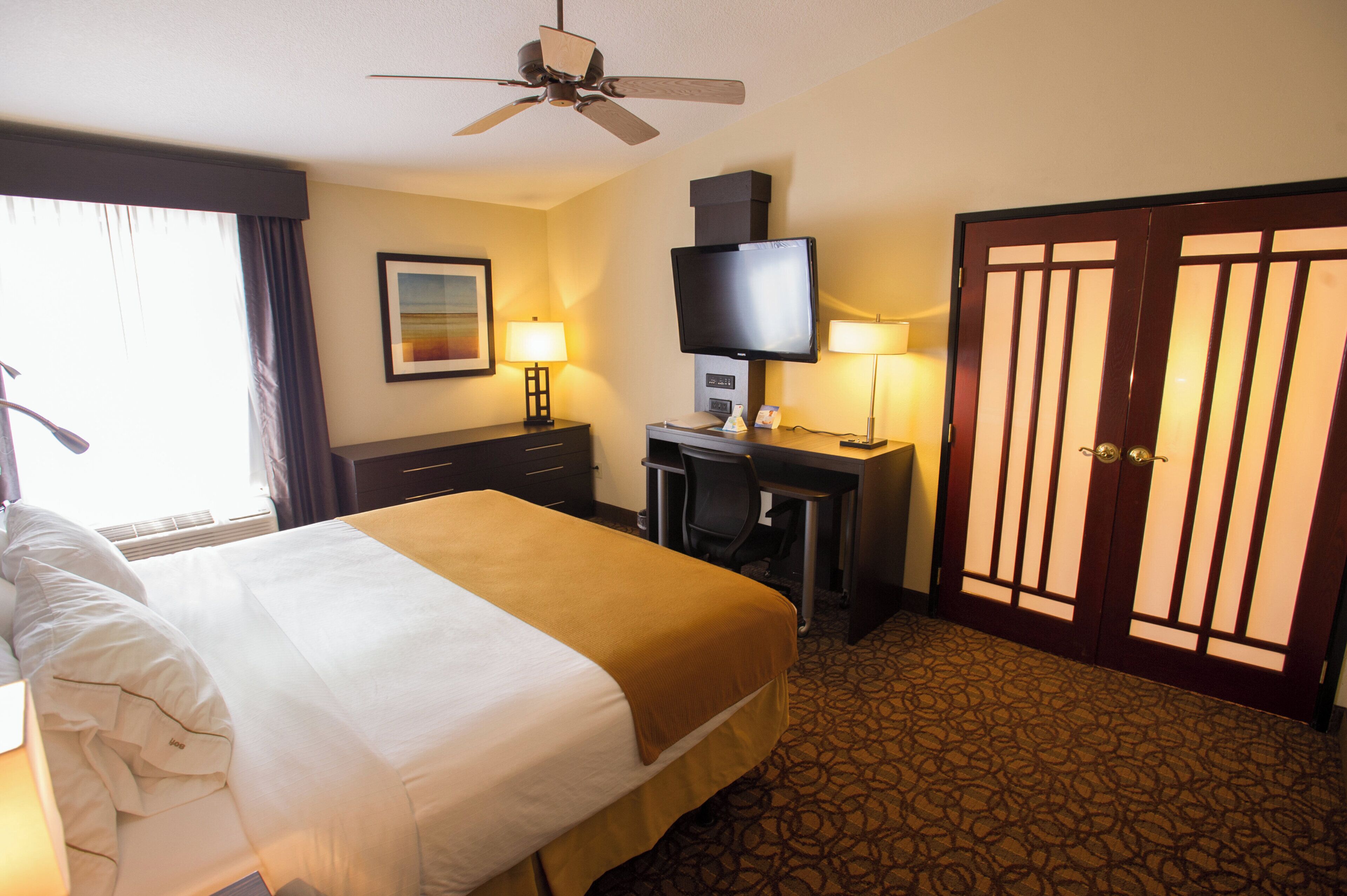 A hotel room with a bed, a desk, a television, and a door.