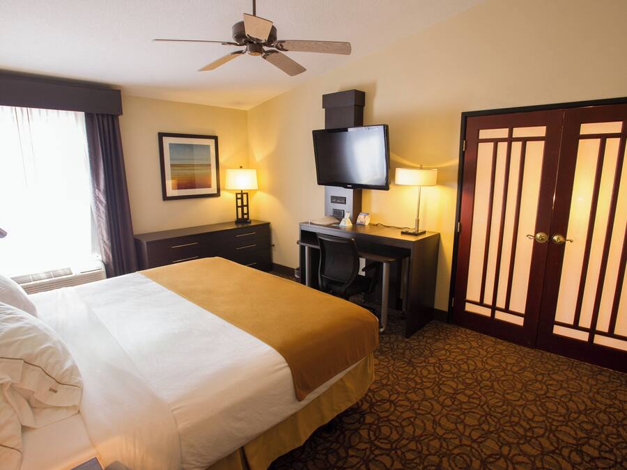 A hotel room with a bed, a desk, a television, and a door.