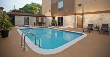A swimming pool with a stone wall and lounge chairs.
