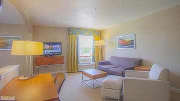 Una habitación de hotel con escritorio, dos sillas, sofá, televisor y ventana con cortinas.