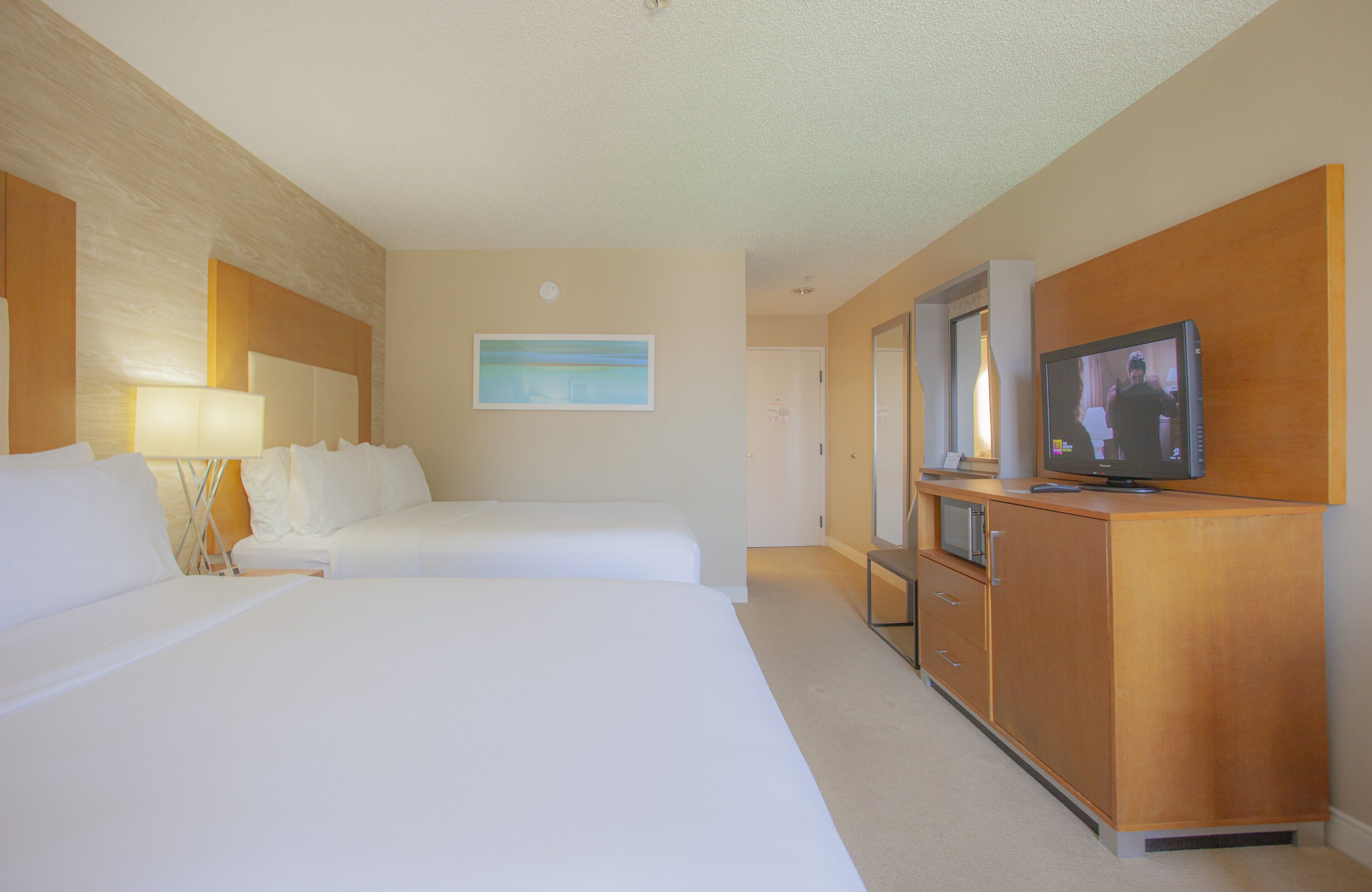 Een hotelkamer met twee bedden, een houten kast, een televisie en een schilderij aan de muur.
