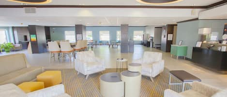 A spacious lobby with multiple seating areas, including sofas and chairs, a reception desk, and a coffee station.