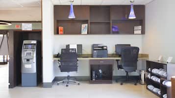 A reception area with an ATM, two office chairs, a desk with a computer, and shelves with folded towels.