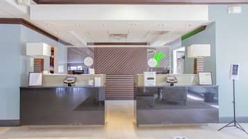 Uma área de recepção com design moderno, com balcão de atendimento, escada e totens de informação digital.