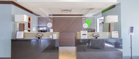 Zona de recepción con diseño moderno, que incluye un mostrador de recepción, una escalera y un quiosco digital de información.