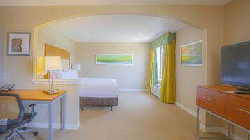 Habitación de hotel con cama, escritorio, silla, televisor y obras de arte en las paredes.