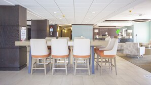A hotel lobby with a reception desk, a dining area with a table and chairs, and a seating area with sofas. - Holiday Inn & Suites Spring- The Woodlands Area by IHG (Spring)