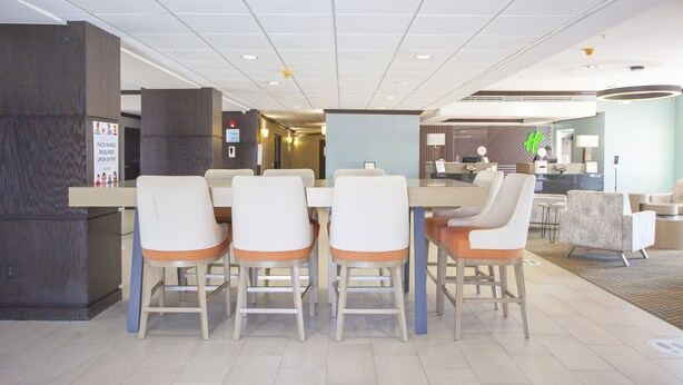 A hotel lobby with a reception desk, a dining area with a table and chairs, and a seating area with sofas. - Holiday Inn & Suites Spring- The Woodlands Area by IHG (Spring)