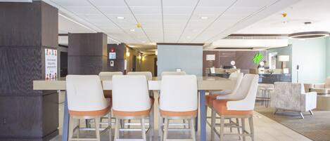 A hotel lobby with a reception desk, a dining area with a table and chairs, and a seating area with sofas.