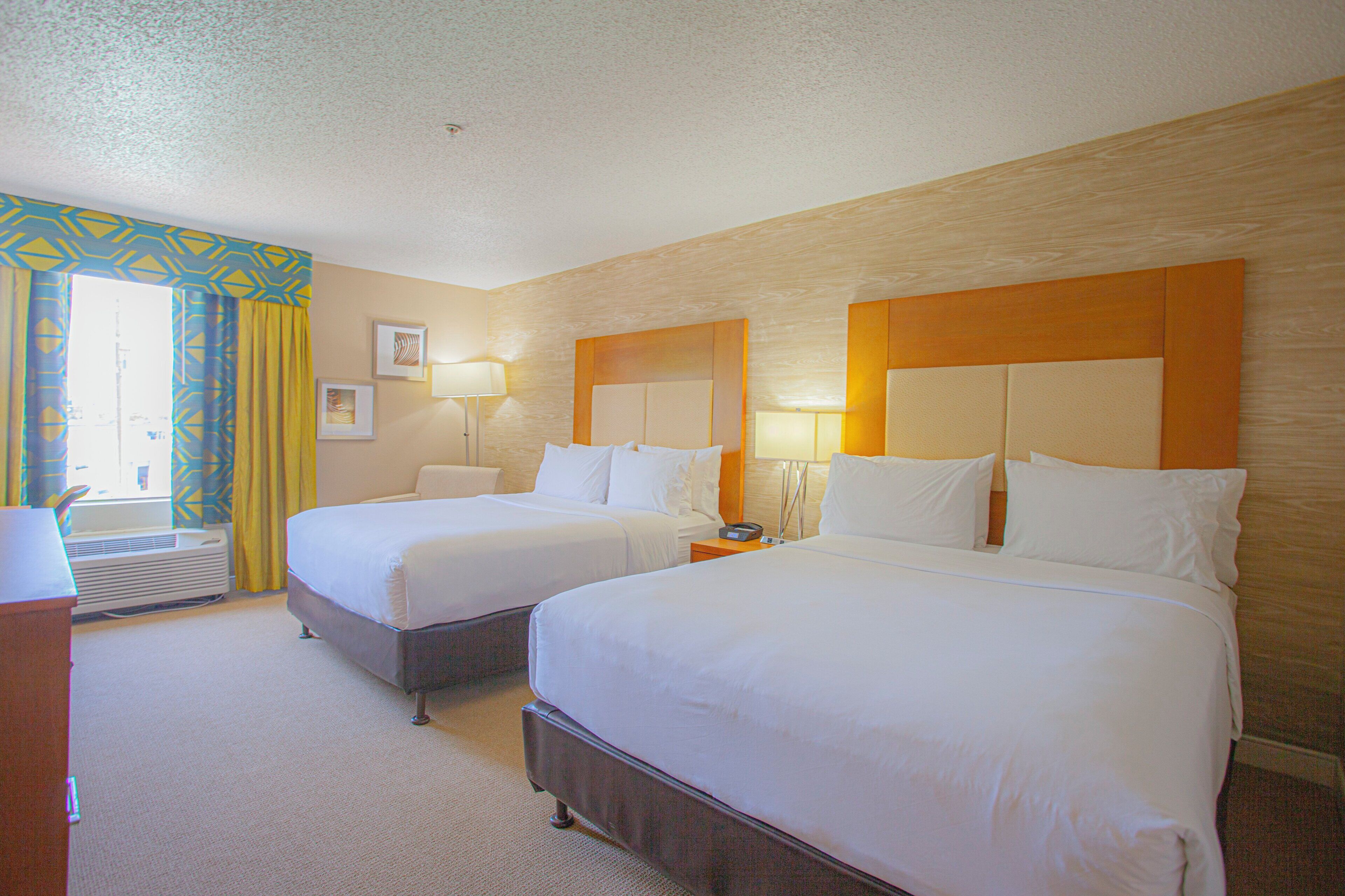 A hotel room with two beds, a desk, and a window with curtains.