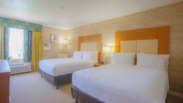 A hotel room with two beds, a desk, and a window with curtains.