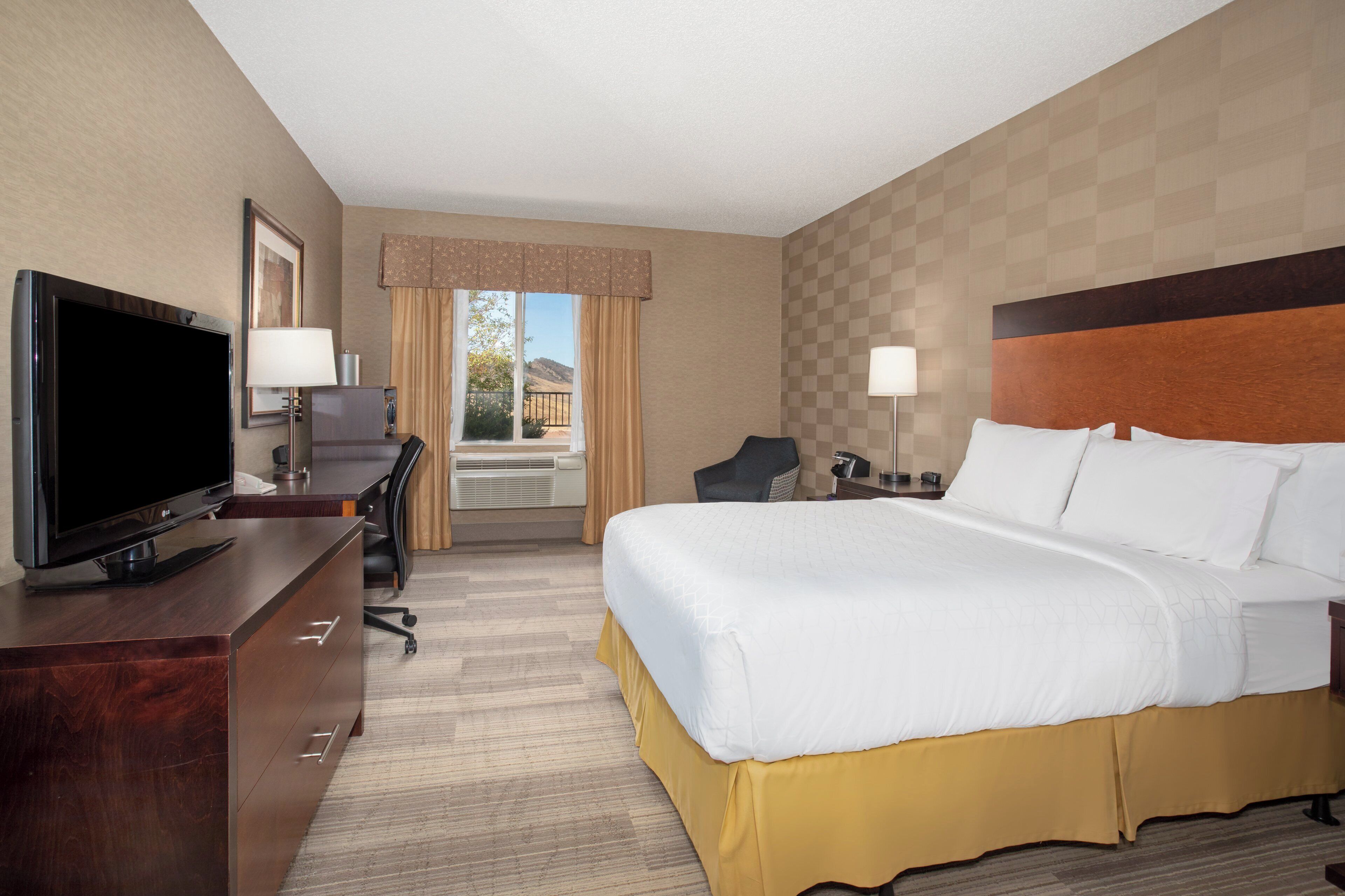 A hotel room with a bed, a desk with a TV, a chair, and a view of the outdoors.