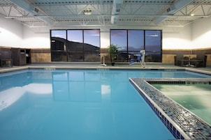 An indoor swimming pool with clear water, a lifeguard stand, and a view of the outside landscape through large windows.