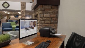 A desktop computer with a monitor, keyboard, and printer on a wooden table in a hotel lobby.