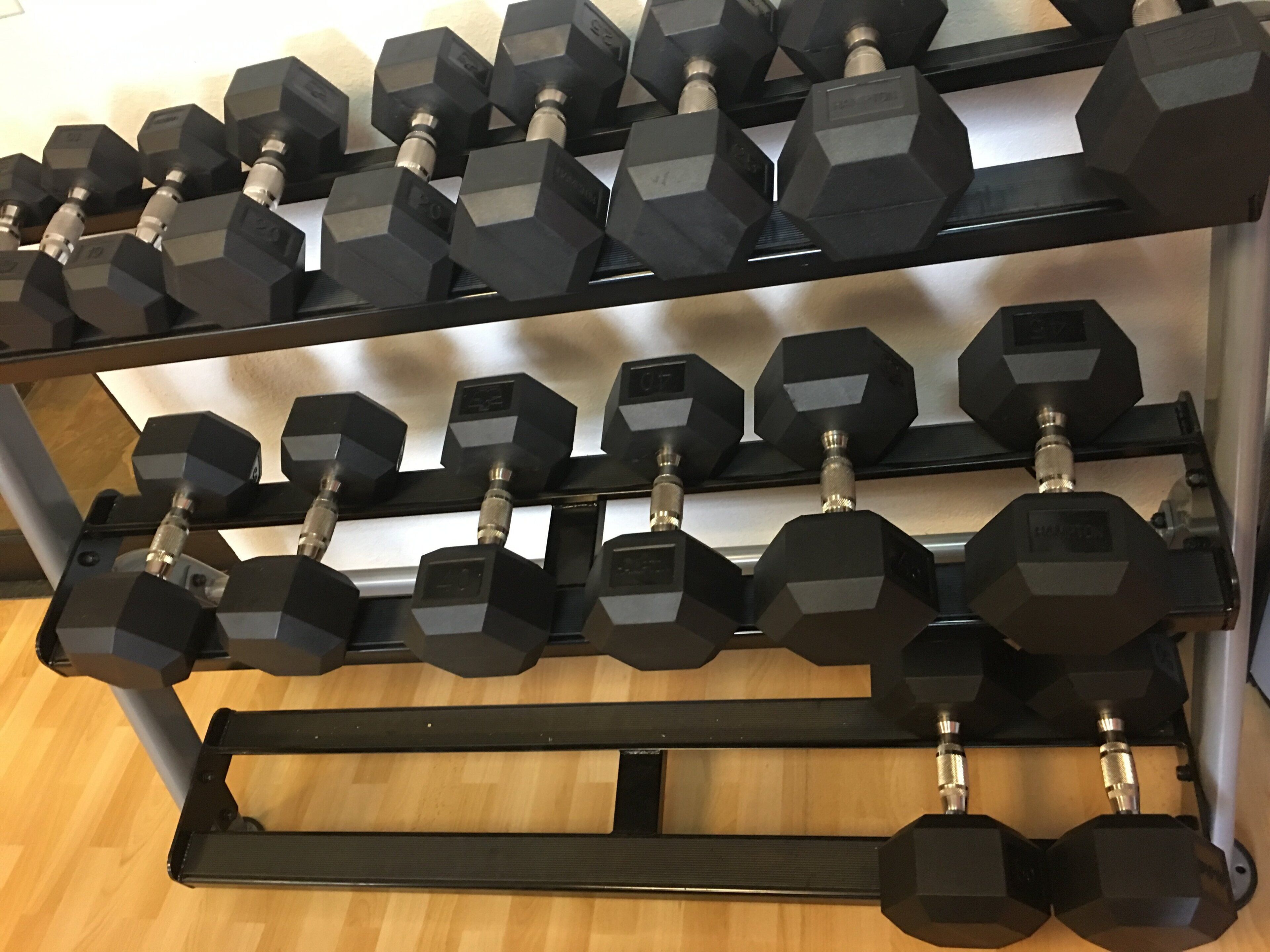 A rack of black hexagonal dumbbells with visible weight markings.