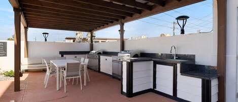 Un espace cuisine extérieur comprenant un comptoir intégré, un barbecue et un ensemble de mobilier de salle à manger.