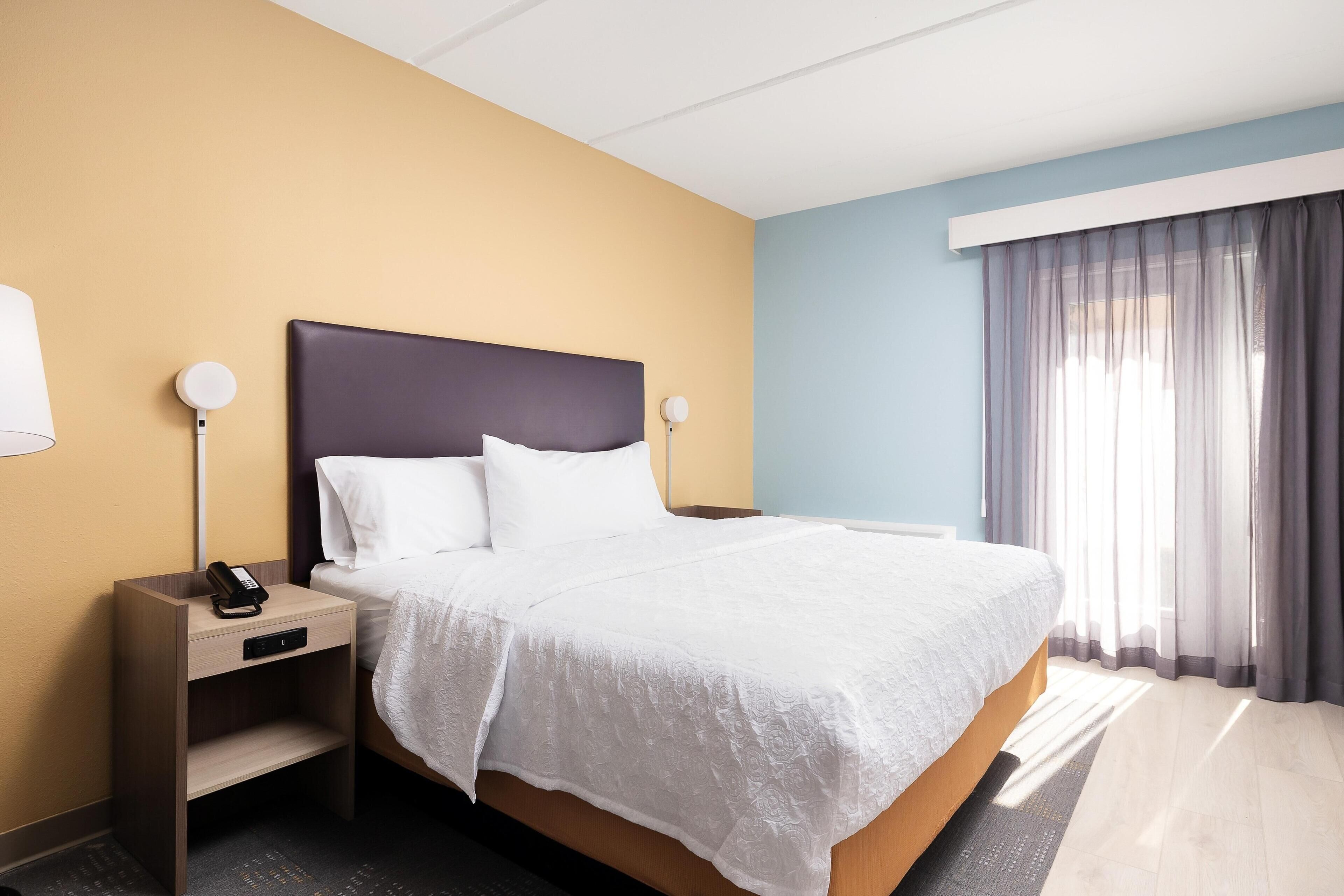 A hotel room with a bed, bedside tables, a lamp, and a window with curtains.