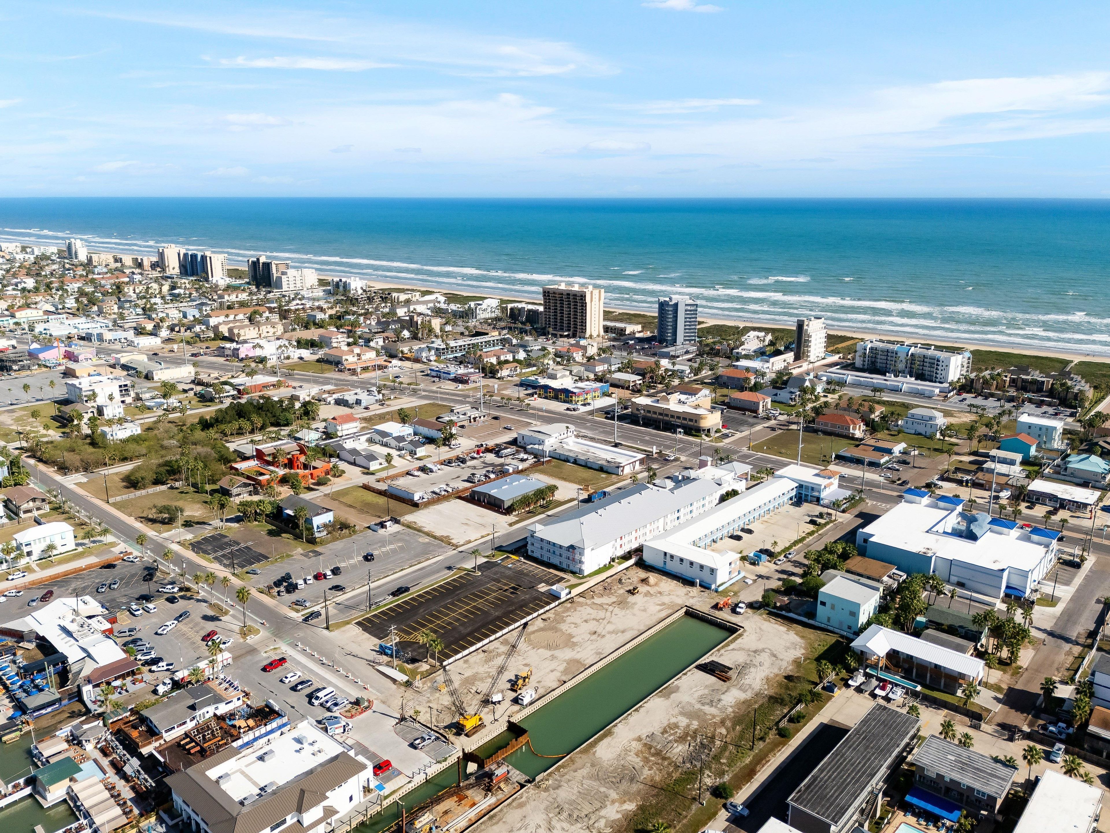 An aerial view of a coastal city with a marina, buildings, and a beach.
